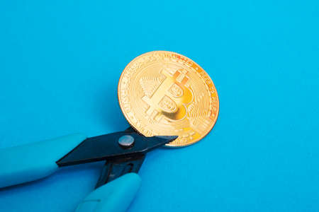 Pliers cut bitcoin coin on a blue background close upの写真素材