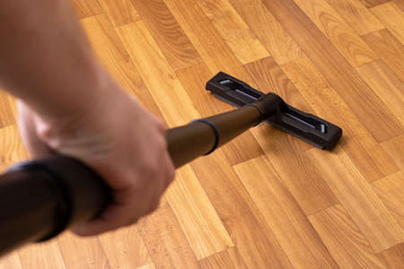 Vacuum cleaner pipe in hand on wooden floor background close upの写真素材