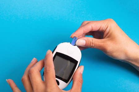 Blood glucose meter in hand on blue background close upの写真素材