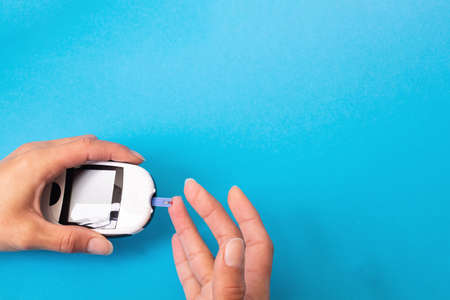 Blood glucose meter in hand on blue background close upの写真素材