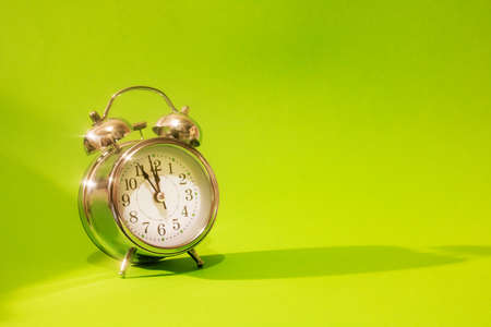 Metal alarm clock on green background in sunlightの写真素材