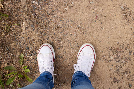 Legs in white sneakers on the sand close upの写真素材