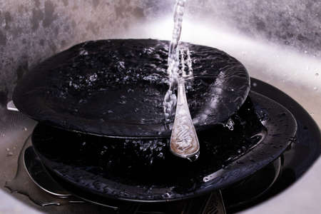 Plates in the sink under the tap close upの写真素材
