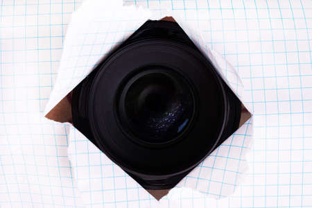 Camera lens in a torn hole in paper close upの写真素材