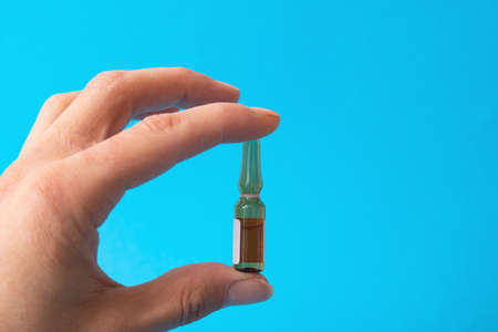 Hand holds ampoule with medicine on blue background close upの写真素材