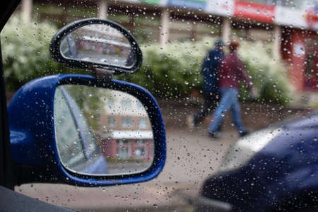 Raindrops on car side view mirror and window close up. bad weather driving