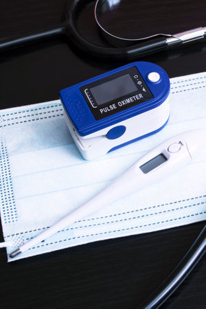 Mask, stethoscope, thermometer and oximeter on black background close up