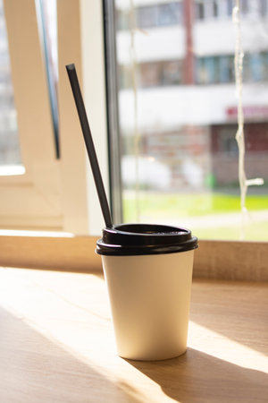 Black paper coffee cup on the table by the windowの写真素材