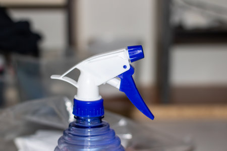 An electric blue and white spray bottle filled with liquid is resting on a table. The bottle contains a waterbased fluid, perfect for cleaning glass and plastic surfacesの写真素材