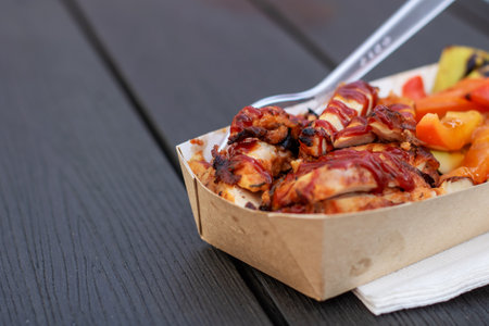 A paper container filled with a Californiastyle pizza topped with chicken, vegetables, and pizza cheese, ready to eat with a plastic fork as fast foodの写真素材