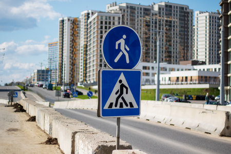 In front of a building under construction, there is a blue and white pedestrian crossing sign. The sky is visible in the backgroundの写真素材