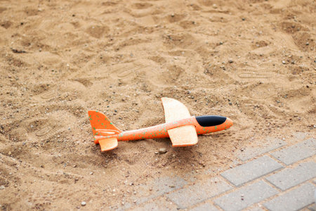 A small orange toy airplane rests on the ground, surrounded by sand. The landscape appears to be a...