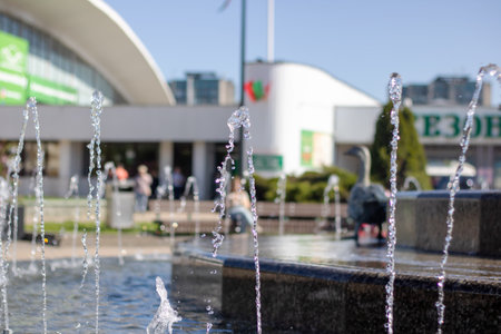A fountain is located in front of a building with the description e3oh. The image depicts water, a fountain, and a public space during the daytimeの写真素材