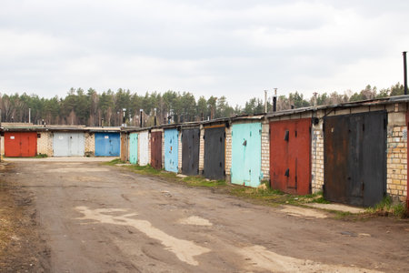 A series of garages are positioned alongside a dusty country road, creating a rustic and scenic...