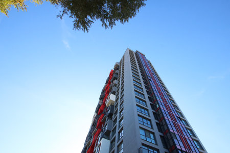 While gazing upwards, I admire a remarkable tall building, set against the backdrop of a vivid blue...