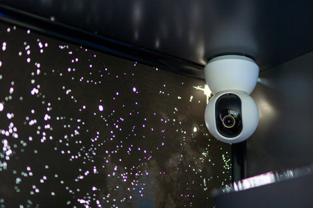 A security camera is positioned and securely hanging from the ceiling in a dark and dimly lit room, monitoring the surroundings continuouslyの写真素材