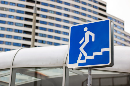 A vibrant blue sign prominently displays an image of a person ascending a set of stairs, guiding individuals on their way to their destinationの写真素材