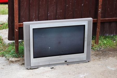 A large television set is positioned on the ground in front of a sturdy fence, creating a scene that combines technology with outdoor elementsの写真素材