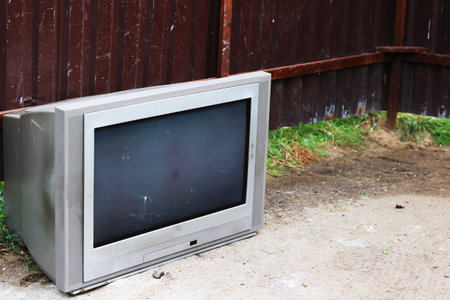A large television set is positioned on the ground in front of a sturdy fence, creating a scene that...