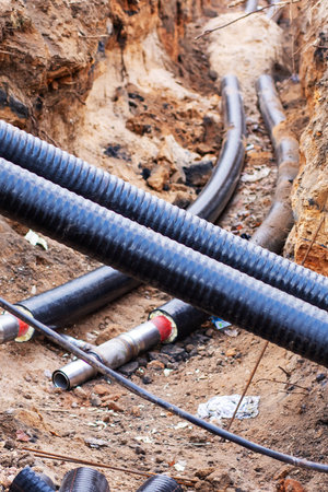 A collection of various pipes is currently resting in the dirt within a trench that has been...