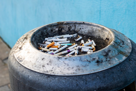 A disorganized pile of used cigarettes rests in an ashtray, set against a vibrant blue wall in the...