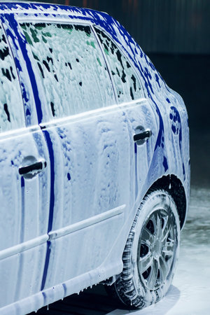 A blue car is meticulously covered in foam while it is being thoroughly washed and cleaned to maintain its appearance and hygieneの写真素材