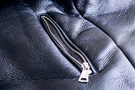 A closeup view of a sleek black leather jacket that showcases luxurious fur trim along with...