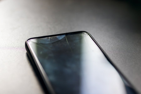 On a table, there is a phone that has a broken screen, showing its damaged state which affects its...