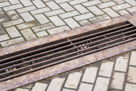 A rusty metal grate is positioned on top of a brick sidewalk, adding an element of texture and complexity to the urban landscape beneathの写真素材