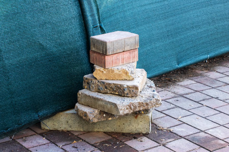 A large pile of bricks is neatly stacked on top of one another on a solid brick sidewalk that...