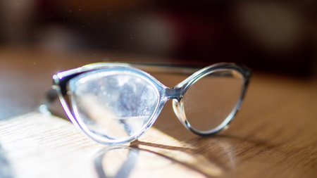 On a beautifully crafted wooden table, there rests a stylish pair of glasses, neatly placed and...