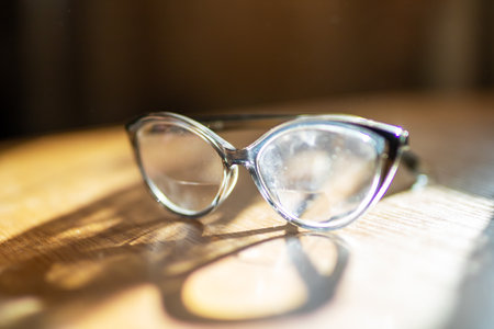 A stylish pair of glasses is resting on top of a beautiful wooden table, showing their elegant design and reflective lensesの写真素材