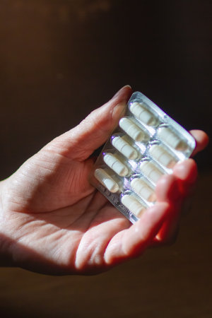 A person is carefully holding a blister pack of various pills in their hand, showing its medical...