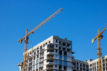 A bustling construction site featuring multiple cranes and a large highrise building that is...