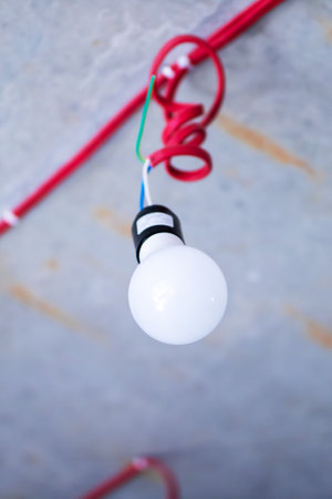 A bright and shiny light bulb is hanging down from a vibrant red cord that adds a pop of color to...