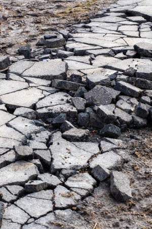 A detailed close up of a significantly cracked and damaged asphalt road surfaceの写真素材