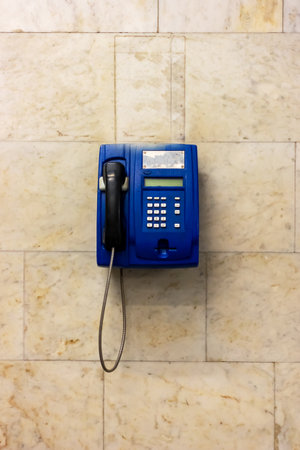 A blue pay phone is currently hanging on a wall nearbyの写真素材