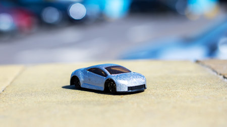 A shiny silver toy car is positioned on a hard concrete surface, resembling the size and shape of a...