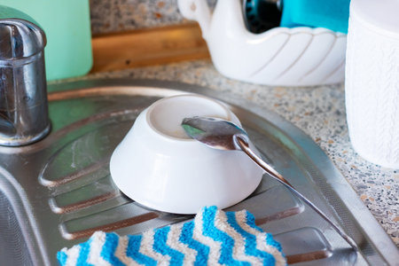 In the kitchen, a bowl containing a spoon is placed inside a sink, waiting to be washed or used...