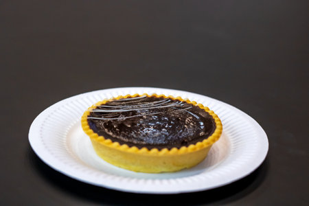 On a pristine white plate sits a delectable chocolate tart, beautifully presented and ready to be...