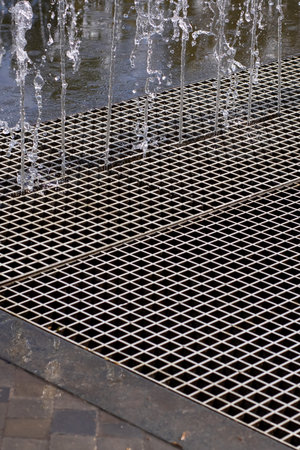 A detailed closeup of a metallic grate that is actively allowing water to flow out from it, creating...