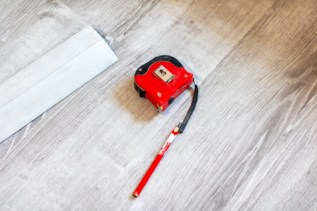 A vibrant red tape measure is resting on a smooth wooden floor adjacent to a pencil, creating an interesting visual contrastの写真素材