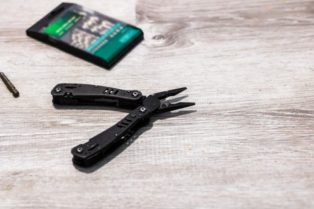 A pair of pliers is placed on a wooden table, conveniently located next to a cell phone that is resting nearbyの写真素材