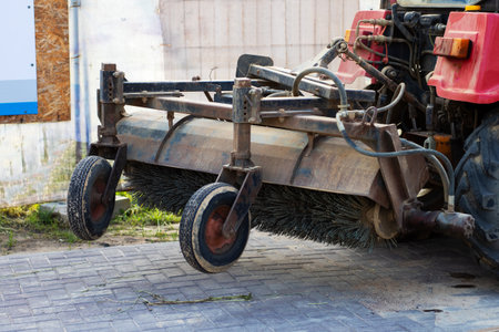 A bright red tractor that has a large broom attached to it for sweeping or cleaning purposes while...
