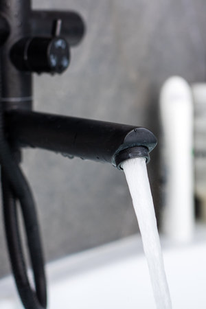 Elegant black faucet dispensing fresh water in a contemporary bathroom setting, showing modern...