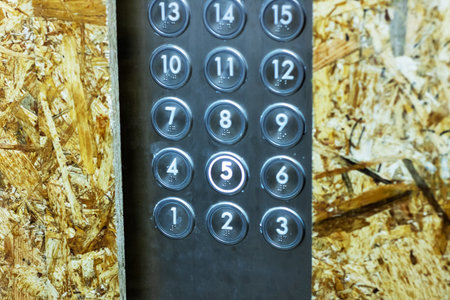 A detailed close-up of a modern elevator keypad on an unfinished wooden surface. Ideal for...