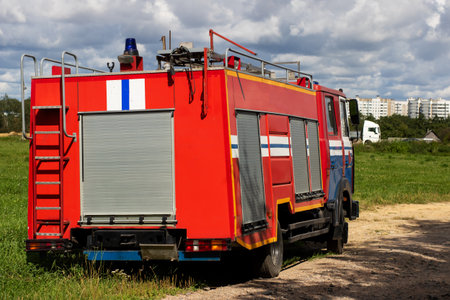A red fire truck parked in a grassy field, showing its unique design and features under a cloudy...