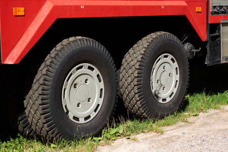 This image features two rugged truck tires mounted on a red vehicle, set against a natural grassy...