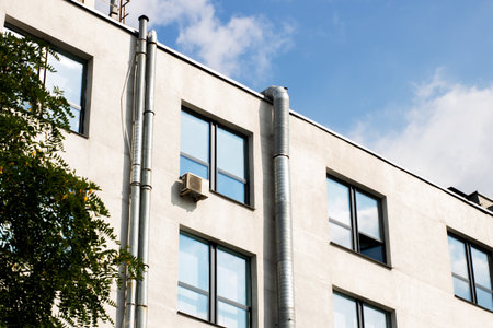 There exists a building characterized by numerous windows and featuring a prominent chimney located...