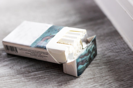 open cigarette pack on wooden table soft window light highlights torn foil and row of filters muted beige and gray tonesの写真素材